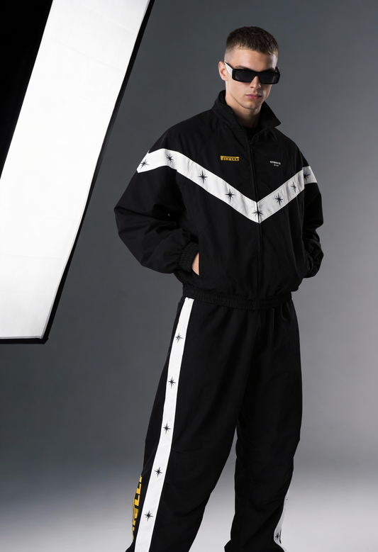 Person wearing a black tracksuit with white stripes and sunglasses on a gray background