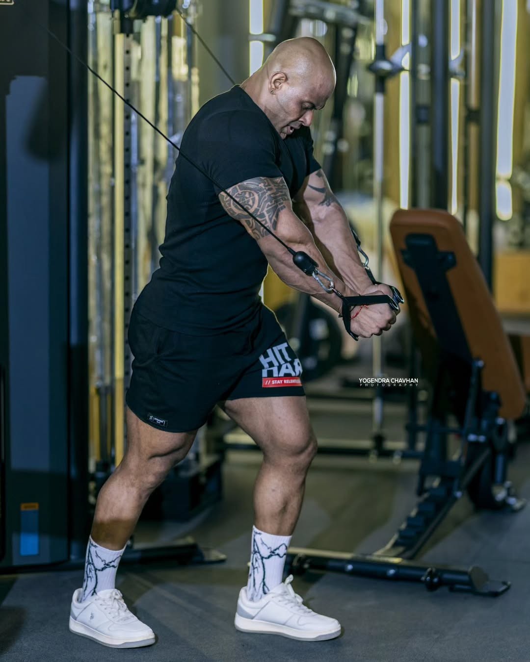 Strong Soul black ribbed slim fit t-shirt and black training shorts worn by a bald man with tattoos working out on a cable machine.